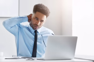 Person sitting at computer holding neck in pain from poor posture and prolonged screen use
